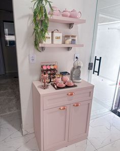 a kitchen with pink cabinets and shelves filled with teacups, coffee cups and other items