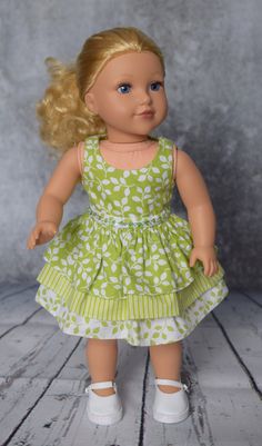 a doll with blonde hair wearing a green dress and white shoes, standing on a wooden floor