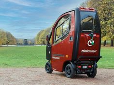 a small red car parked on top of a dirt road next to a lush green field