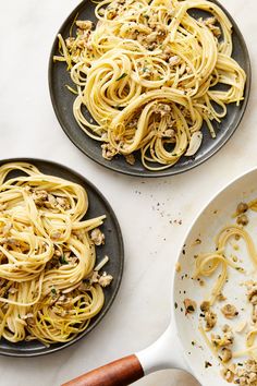 two black plates filled with pasta and meat on top of a white table next to a wooden spatula