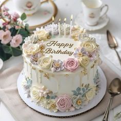 a birthday cake with flowers and candles on it sitting on a table next to silverware