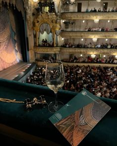 a glass of wine sitting on top of a table in front of a stage filled with people