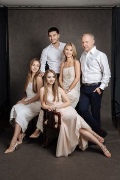 a group of people posing for a photo in front of a gray background with one woman sitting on a chair