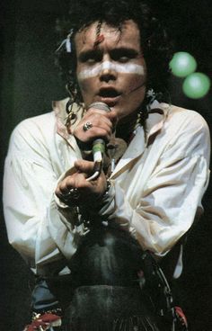 a man with his face painted white holding a microphone and wearing chains on his neck