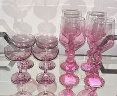 a table topped with lots of pink wine glasses and dishes on top of a glass shelf