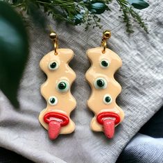 a pair of yellow earrings with green eyes and red tongue hanging from it's hooks