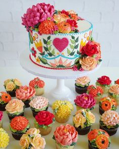 cupcakes with flowers and hearts on them sitting next to a cake