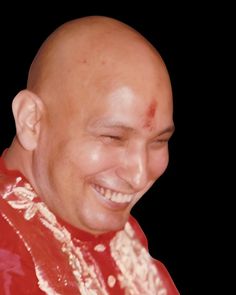 a bald man smiling and wearing a red shirt with white trim on his head, in front of a black background