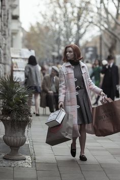 a woman with red hair carrying shopping bags and walking down the street in front of people