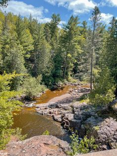 a river running through a forest filled with lots of rocks and green trees in the background