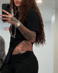 a woman with long hair and tattoos taking a selfie in front of a mirror