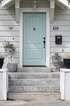 a blue front door with two planters on the steps next to it and an entry way