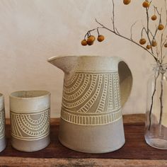 three vases sitting on top of a wooden table next to a glass vase with berries in it