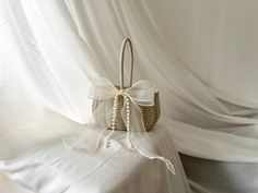 a white basket with a bow on it sitting on top of a bed next to a curtain