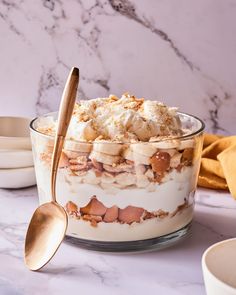 a dessert dish with bananas and whipped cream in it on a marble counter top next to two gold spoons