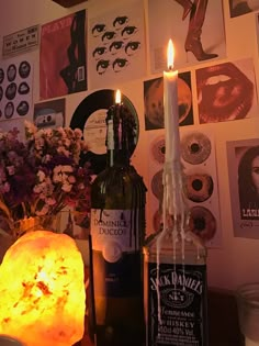 two bottles with candles sitting next to each other in front of pictures on the wall