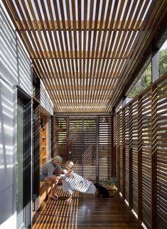 a person sitting on a bench under a wooden pergolated roof with sunlight streaming through it