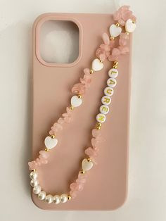 a pink phone case with pearls and beads on the front, sitting on a white surface