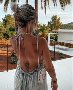 a woman with tattoos on her back standing next to a palm tree