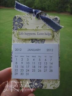 a hand holding up a small calendar with a blue bow on it's end