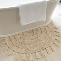 a white bath tub sitting on top of a bathroom floor next to a rug with tassels