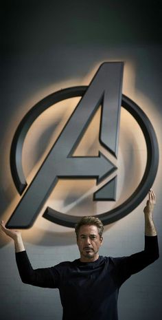 a man standing in front of the avengers logo with his hands up and arms raised