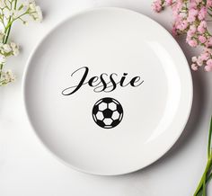 a white plate with a soccer ball and name on it next to some pink flowers