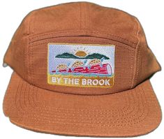 a brown hat with the words by the brook on it and an image of a boat