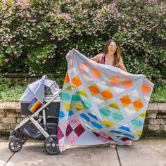 a woman holding up a quilt next to a stroller