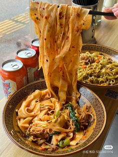 two plates filled with noodles and vegetables next to cans of soda