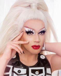 a woman with long white hair and black eye makeup is posing for the camera while holding her hand near her face