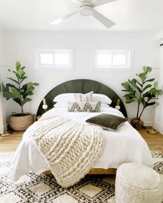 a bedroom with white walls, black and white bedding, potted plants and pillows