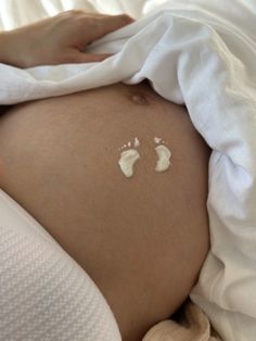 a pregnant belly with two baby footprints on it's side and white sheets around it