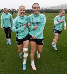 three women in soccer uniforms are walking on the field together and smiling at the camera