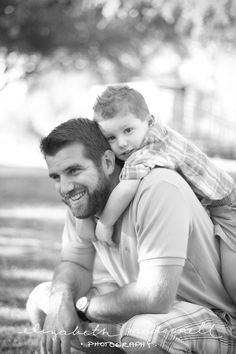 a man holding a little boy in his arms while sitting on the ground under a tree