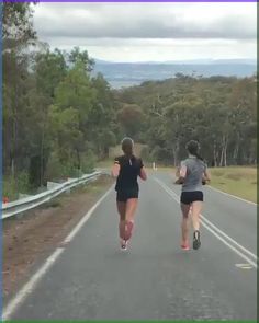 two women running down the road with trees and hills in the background on either side