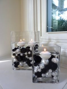 two clear vases with white and black balls in them on a table next to a window