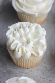 three cupcakes with white frosting sitting on a table