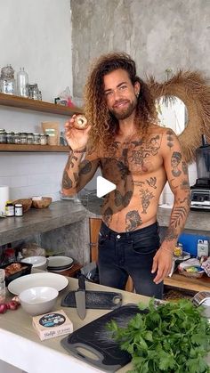 a man with long hair standing in a kitchen next to a counter holding a knife