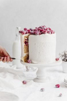 someone is cutting into a cake with white frosting and raspberries on top