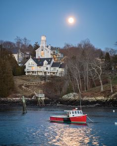 a red and white boat floating on top of a lake next to a large house