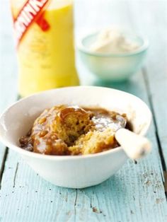 a white bowl filled with pudding next to a bottle of orange juice and a spoon