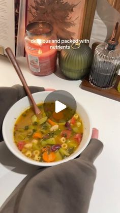 a person holding a bowl of soup in front of a book on a table with candles