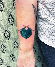 a woman's arm with a green heart tattoo on the left side of her wrist