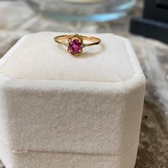 a gold ring with a pink tourmaline stone sits on a white velvet box