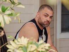 a man sitting on a porch next to a potted plant and looking at the camera