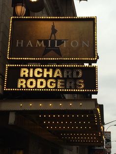 a large sign that is hanging from the side of a building with lights on it