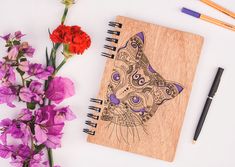 a wooden notebook with an image of a cat on it next to flowers and pens