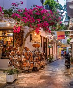 the street is lined with shops and decorated with pink bougaia trees in bloom