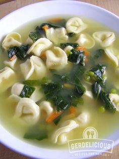 a white bowl filled with tortellini soup on top of a wooden table